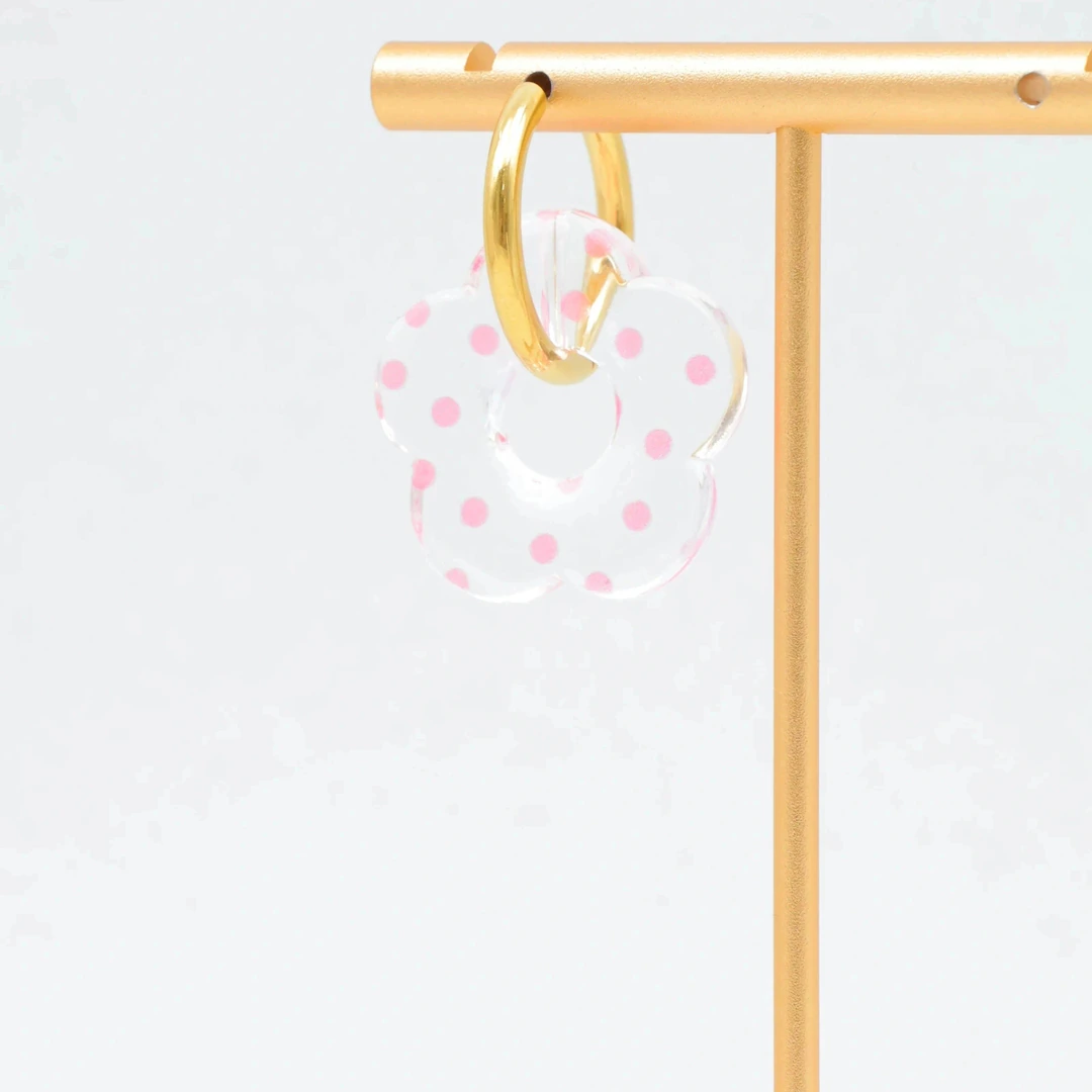 Créole dorée à pendentif fleur transparente à pois roses suspendue à un présentoir doré