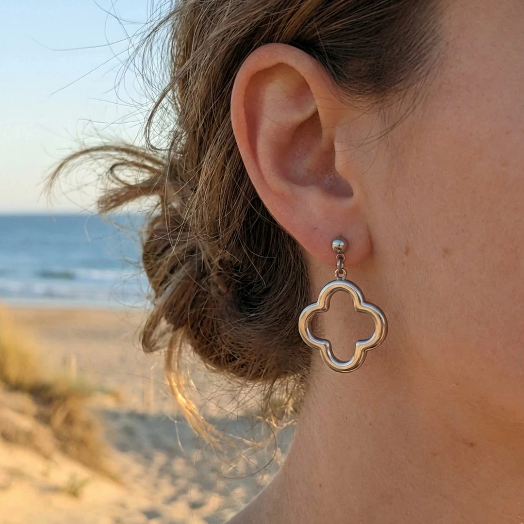 Boucles d'oreilles pendantes argentées motif trèfle ajouré sur puce boule, portées à l'oreille à la plage
