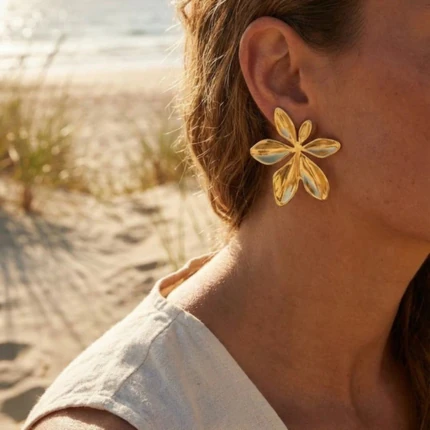 Boucles d'oreilles femme dorées grande fleur à pétales en relief portées à l'oreille à la plage
