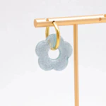 Créole dorée à pendentif fleur bleu clair translucide et pailletée sur un présentoir doré