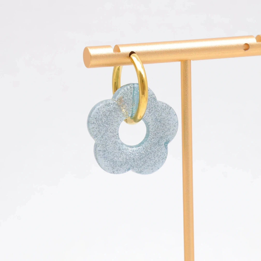 Créole dorée à pendentif fleur bleu clair translucide et pailletée sur un présentoir doré
