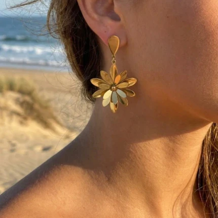 Boucles d'oreilles pendantes dorées fleur à pétales allongés sur attache goutte, portées à l'oreille