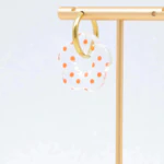 Créole dorée à pendentif fleur translucide à pois orange suspendue à un présentoir doré