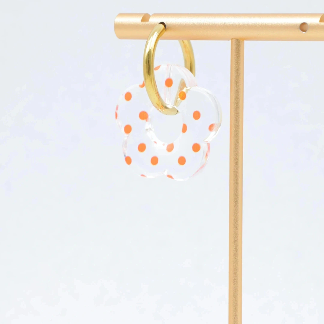 Créole dorée à pendentif fleur translucide à pois orange suspendue à un présentoir doré