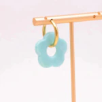 Créole dorée à pendentif fleur bleu ciel à cinq pétales suspendue à un présentoir doré