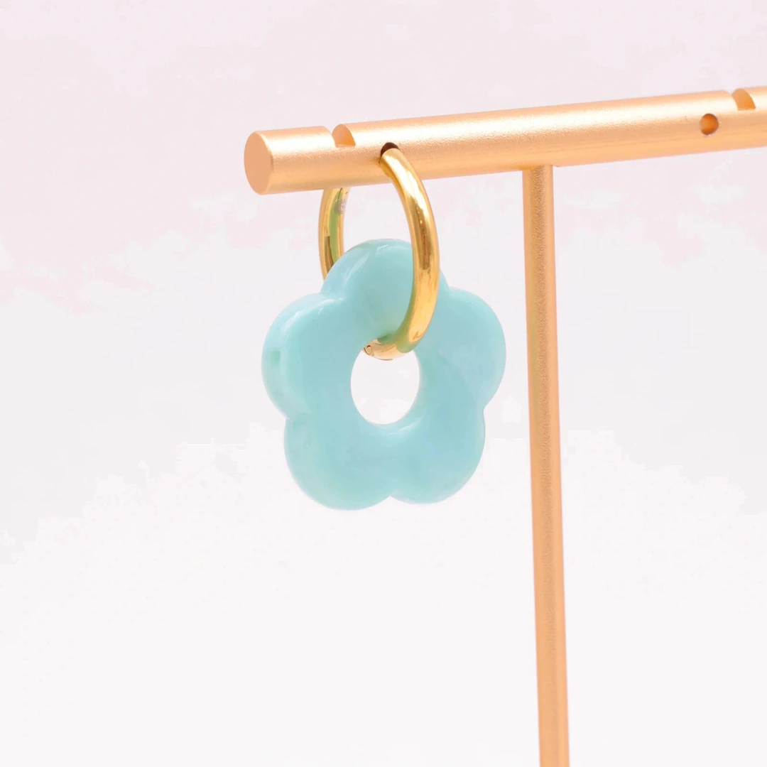 Créole dorée à pendentif fleur bleu ciel à cinq pétales suspendue à un présentoir doré