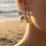 Boucles d'oreilles femme argentées grande fleur à pétales en relief portées à l'oreille, plage en fond