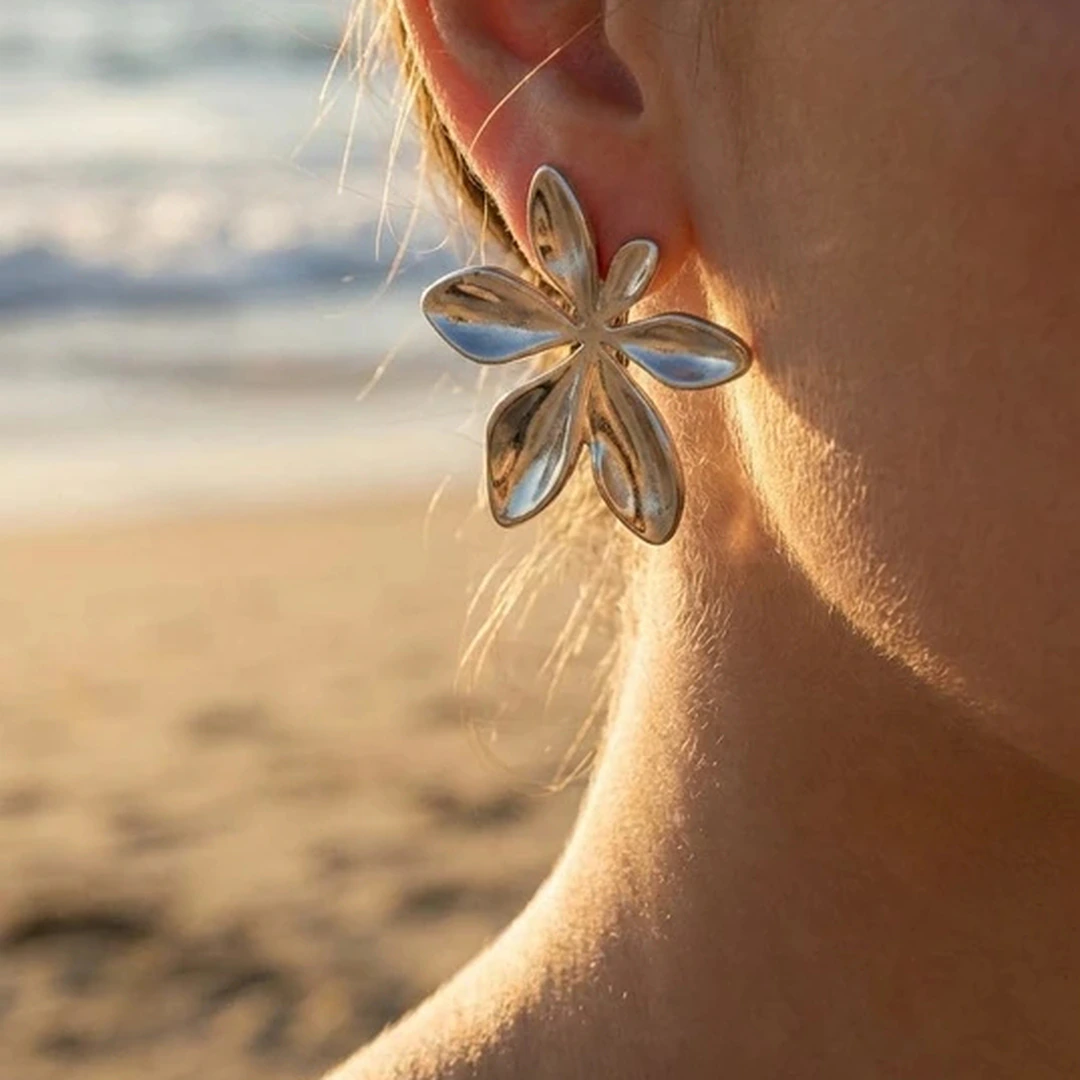 Boucles d'oreilles femme argentées grande fleur à pétales en relief portées à l'oreille, plage en fond