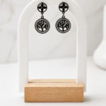 Boucles d'oreilles pendantes arbre de vie noir cerclé de strass et puce trèfle sur présentoir arche blanc