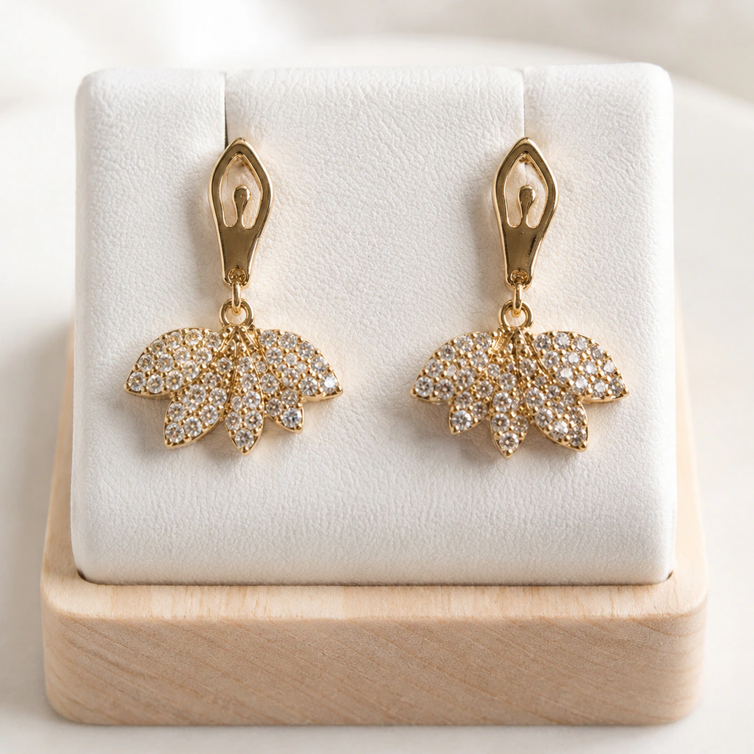 Boucles d'oreilles pendantes dorées fleur scintillante pavée de strass sur un présentoir blanc et bois