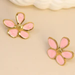 Paire de boucles d'oreilles fleur rose poudré au contour doré et centre texturé posées sur fond beige