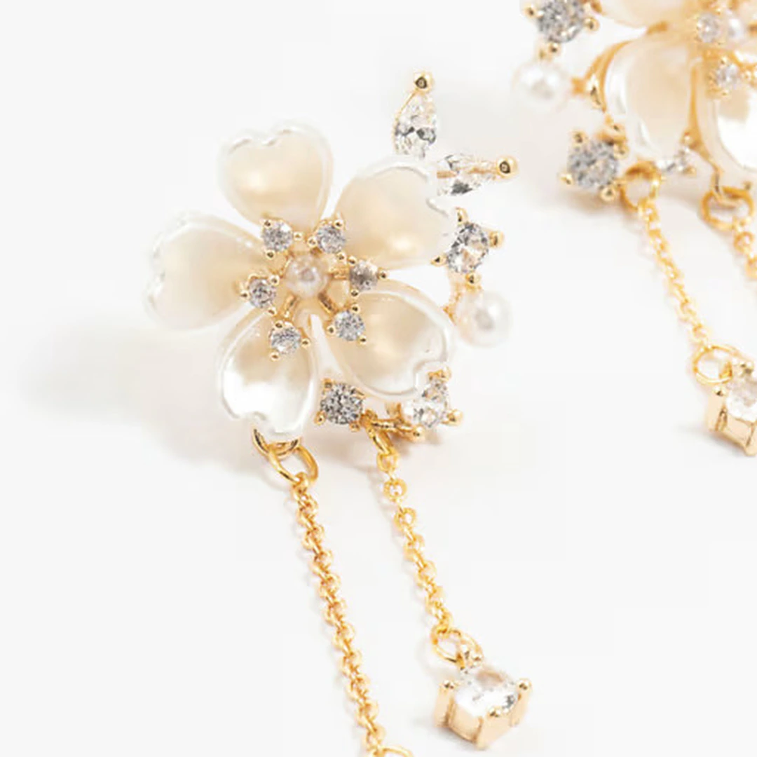 Gros plan sur la fleur nacrée ornée de strass et d'une petite perle, chaînettes dorées et pampille cristal