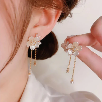 Boucles d'oreilles pendantes fleur nacrée dorées à chaînettes et perle, une portée et une tenue en main