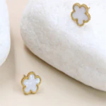 Clous d'oreilles fleur blanche nacrée à bordure dorée perlée, l'un posé sur un galet blanc