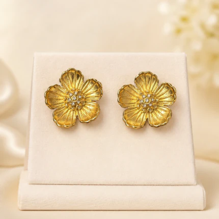 Boucles d'oreilles clous fleur dorée texturée à centre serti de strass sur présentoir crème