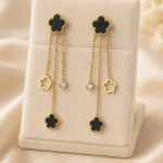 Boucles d'oreilles pendantes fleur noire dorées à fines chaînes, fleur ajourée et strass, sur présentoir
