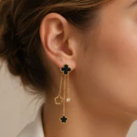 Boucle d'oreille pendante portée à l'oreille : clou trèfle noir, chaînes dorées à charms fleur et strass