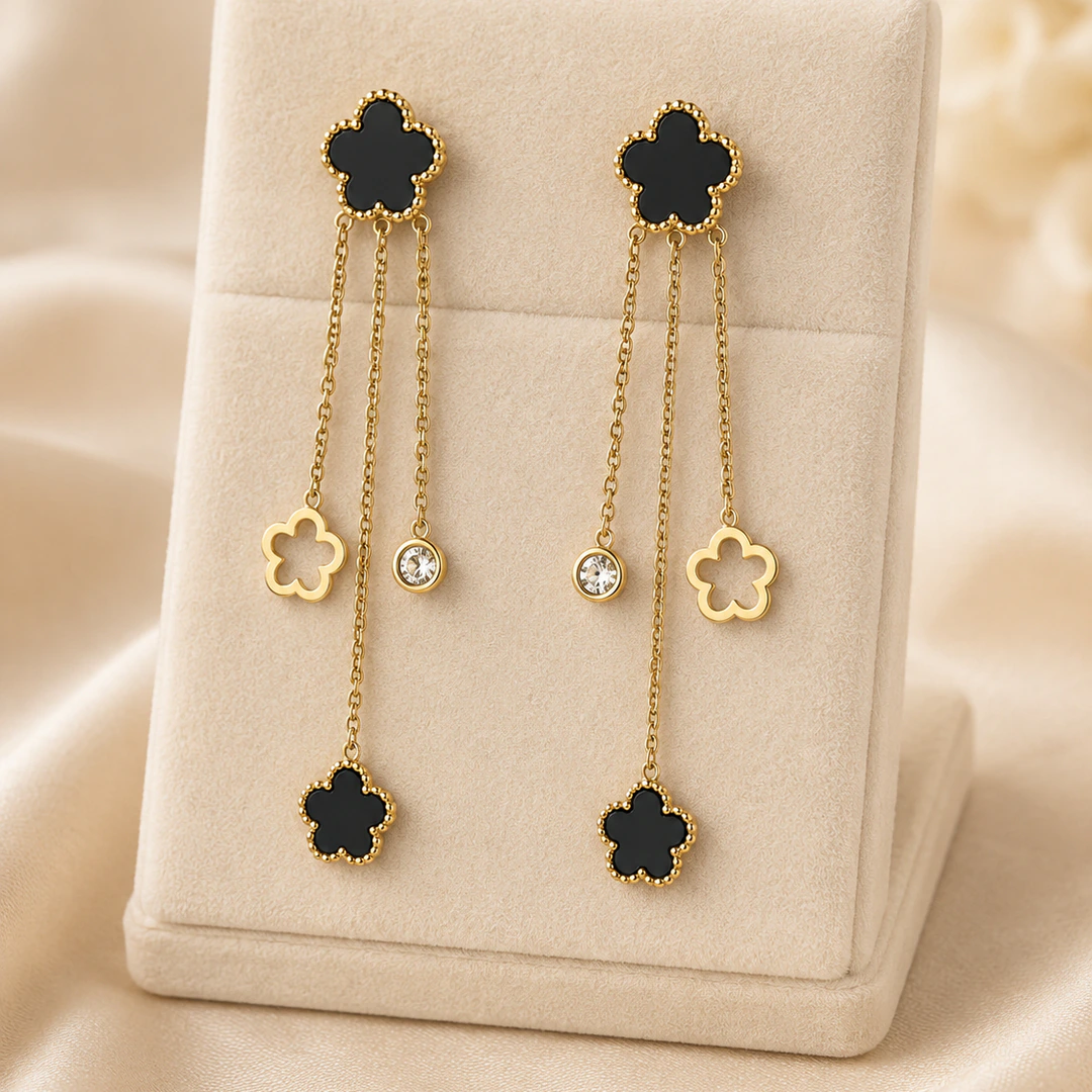 Boucles d'oreilles pendantes fleur noire dorées à fines chaînes, fleur ajourée et strass, sur présentoir