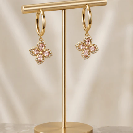 Boucles d'oreilles créoles dorées à pendentif trèfle en cristaux roses et strass sur présentoir