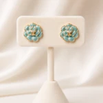 Boucles d'oreilles clous fleur turquoise dorées femme à centre orné de strass sur présentoir crème