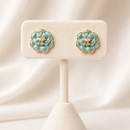 Boucles d'oreilles clous fleur turquoise dorées femme à centre orné de strass sur présentoir crème