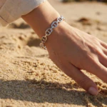 Bracelet jonc ouvert argenté femme à maillons ovales porté au poignet, main posée sur le sable