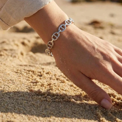 Bracelet jonc ouvert argenté femme à maillons ovales porté au poignet, main posée sur le sable