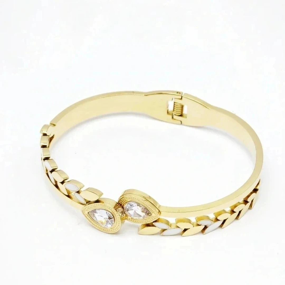 Bracelet jonc doré à charnière, rameau de feuilles blanches et deux cristaux en goutte sur fond blanc