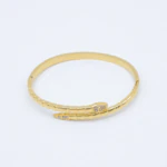 Bracelet jonc doré serpent enroulé à écailles, tête et queue serties de strass sur fond blanc