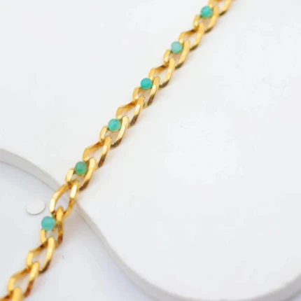 Gros plan sur les maillons dorés et petites perles turquoise du bracelet posé sur un support blanc