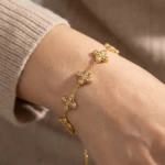 Bracelet trèfle doré à cristaux brillants porté au poignet avec un pull en maille beige