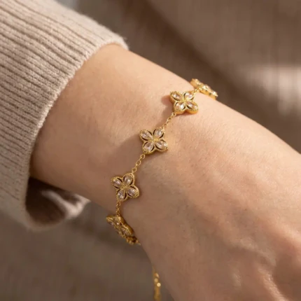 Bracelet trèfle doré à cristaux brillants porté au poignet avec un pull en maille beige