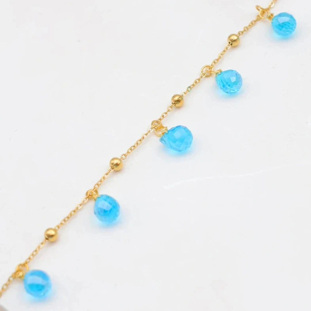 Gros plan sur la chaîne dorée perlée et les gouttes bleu clair facettées du bracelet