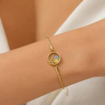 Bracelet doré fin femme à médaillon rond serpent, fleur et mauvais œil bleu porté au poignet