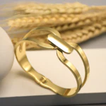 Bracelet manchette doré femme à double bande ajourée et maillon central, posé près d'épis de blé