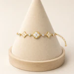 Bracelet chaîne dorée à médaillon trèfle blanc, étoiles blanches et strass sur un présentoir cône
