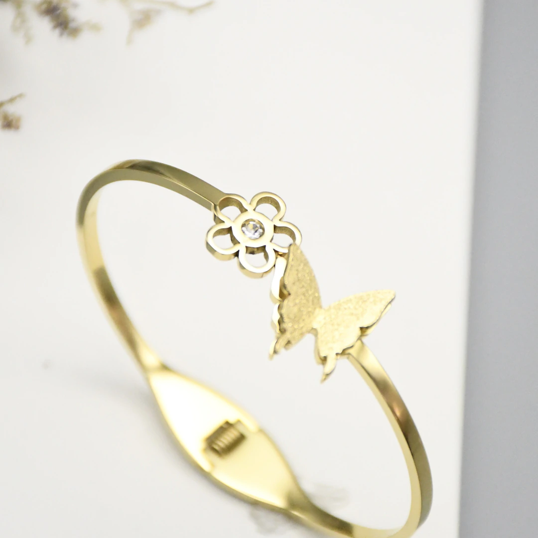 Vue rapprochée du jonc doré à charnière : fleur ajourée à strass et papillon effet sablé