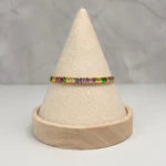 Bracelet doré à cristaux rectangulaires multicolores posé sur un présentoir cône beige