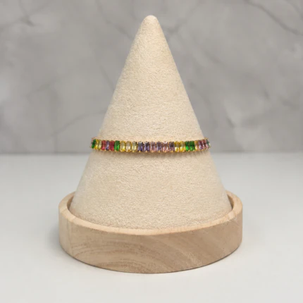 Bracelet doré à cristaux rectangulaires multicolores posé sur un présentoir cône beige