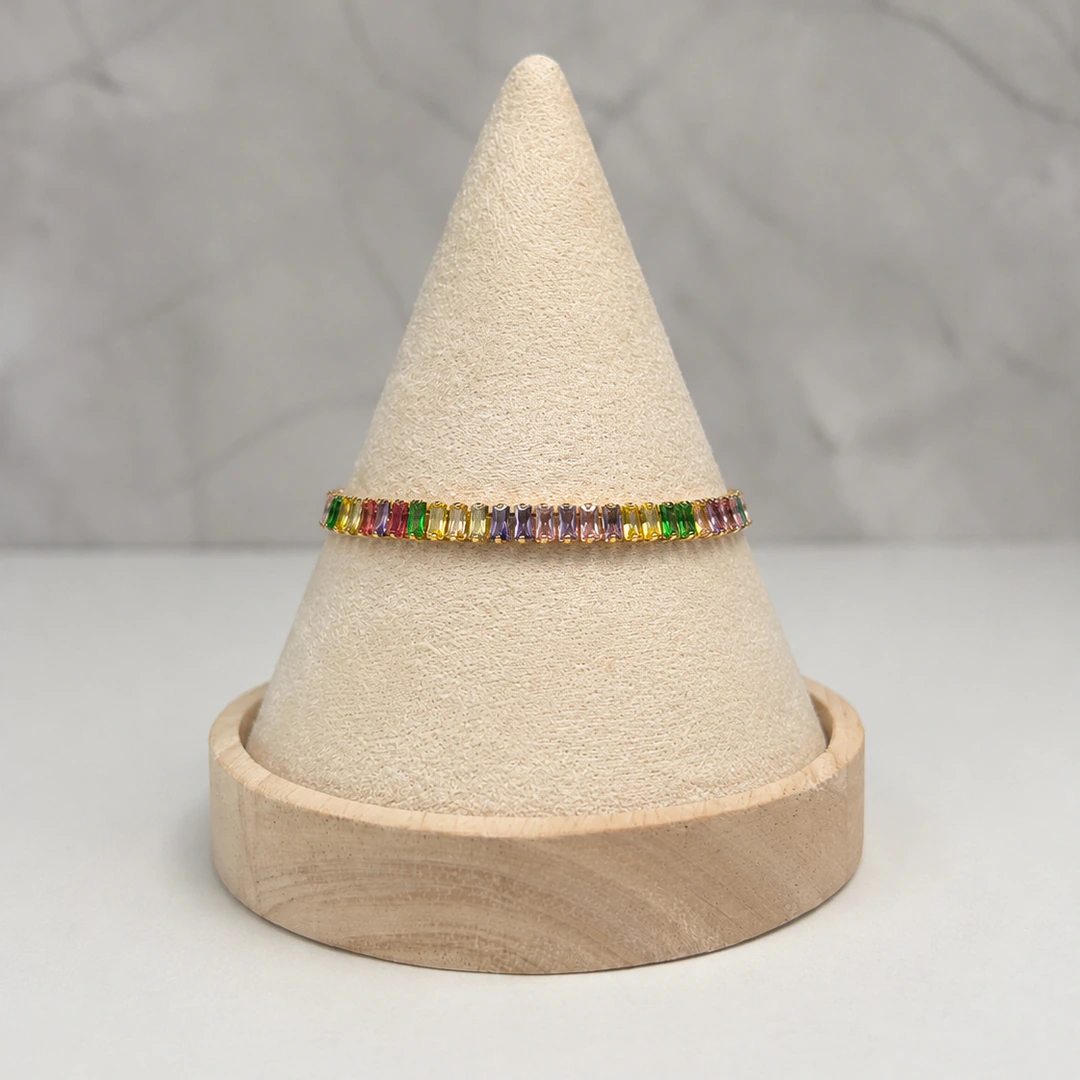 Bracelet doré à cristaux rectangulaires multicolores posé sur un présentoir cône beige