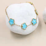 Motifs fleur bleu turquoise effet marbré du bracelet doré posé sur un galet blanc