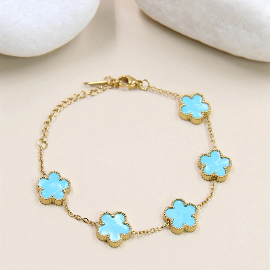 Bracelet chaîne fine dorée femme à cinq motifs fleur bleu turquoise au contour perlé, près de galets