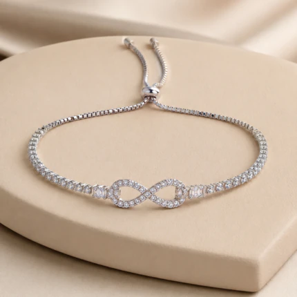 Bracelet argenté femme ajustable à motif infini pavé de strass et fermoir coulissant, sur socle beige