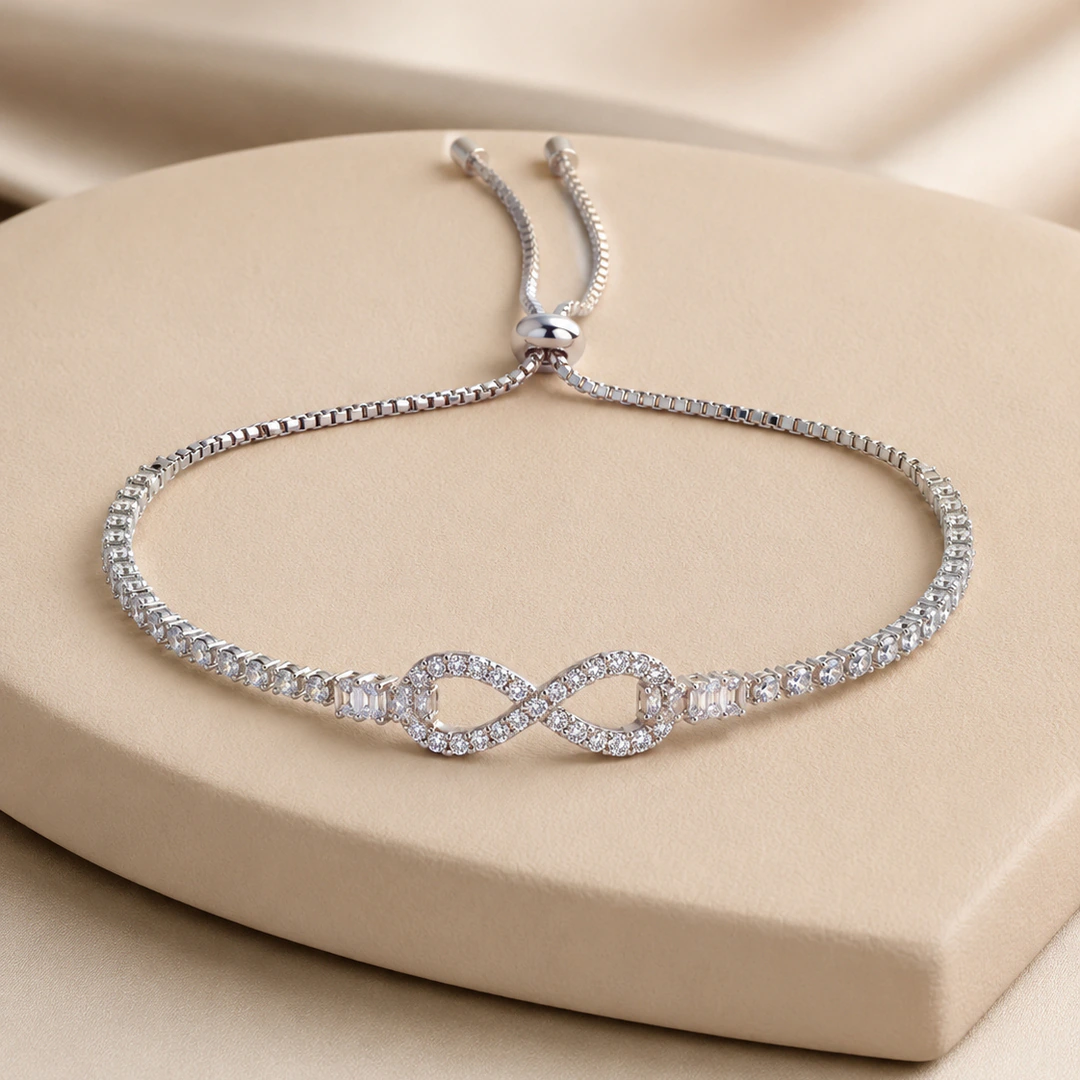 Bracelet argenté femme ajustable à motif infini pavé de strass et fermoir coulissant, sur socle beige