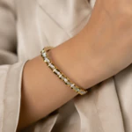 Bracelet jonc doré ondulé pavé de strass porté au poignet avec une tenue satinée beige