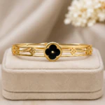 Bracelet jonc doré femme ajouré à trèfle noir central posé sur un écrin en velours beige