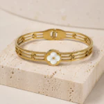 Bracelet jonc doré femme ajouré à trèfle blanc nacré posé sur un bloc de pierre beige