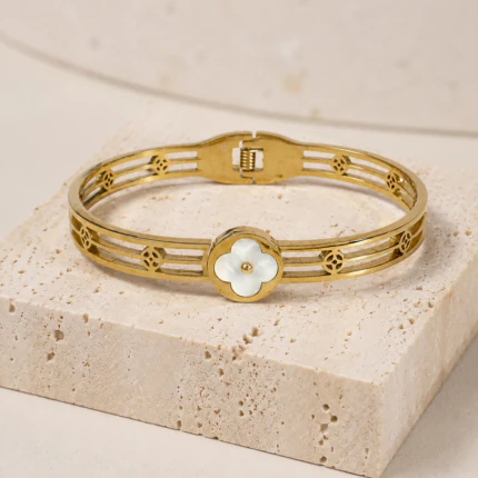 Bracelet jonc doré femme ajouré à trèfle blanc nacré posé sur un bloc de pierre beige
