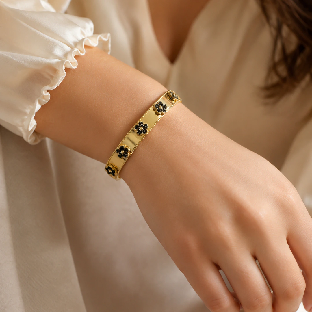 Femme en chemisier à volants portant un bracelet jonc doré à fleurs noires