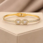 Bracelet jonc doré femme motif infini à deux gouttes en cristal et rangée de pierres claires, sur velours beige
